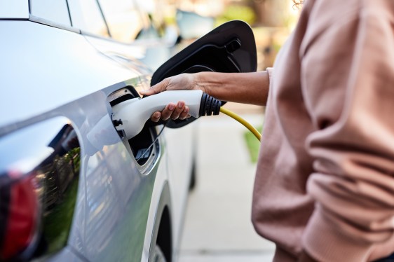 Midsection of woman plugging cable in electric car for charging at back yard