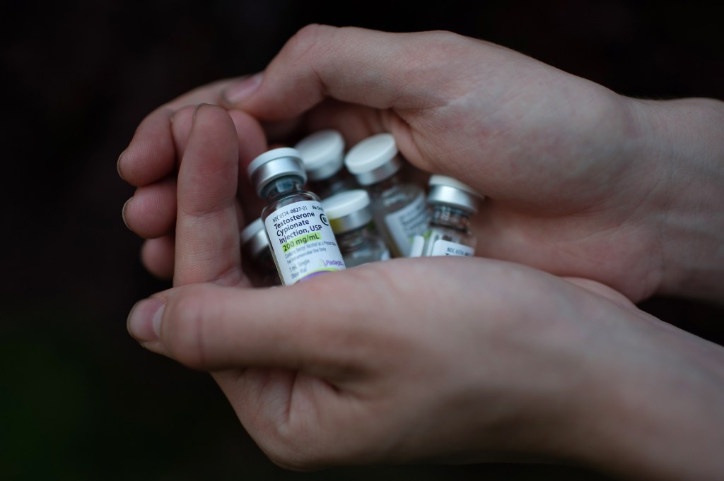 Hands holding several testosterone vials.