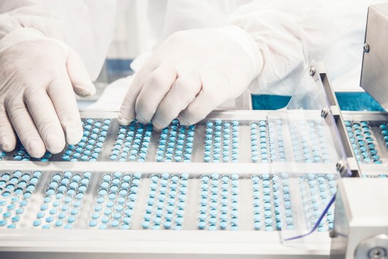 Worker inspecting pills on blisterpack conveyer belt