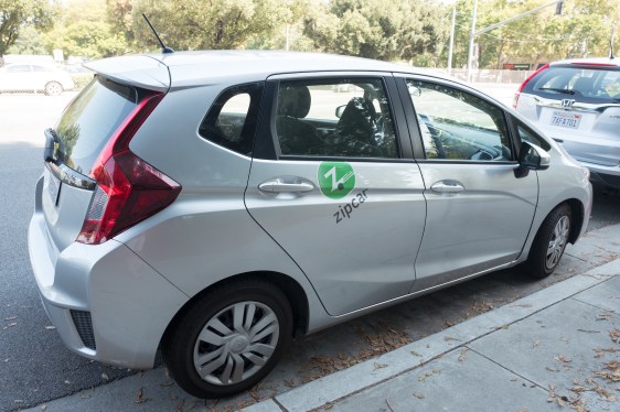 A compact Zipcar car parked beside a curb.