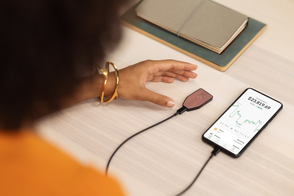 An image of a woman plugging her Trezor Safe 3 crypto hardware wallet into her phone