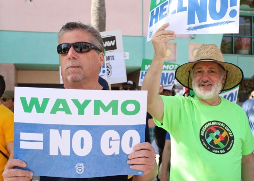 Men holding signs that say WAYMO = NO GO in all caps.
