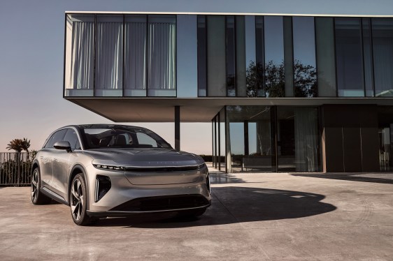 A promotional shot shows a silver Lucid Gravity SUV parked in front of a modern house with big glass windows.