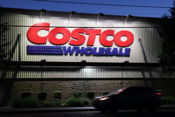 A car passes by a Costco store in Seattle, it's dark and the Costco sign on the warehouse wall is lit up