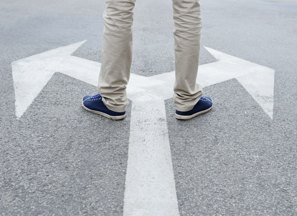 Man standing on two arrows on road going in opposite directions