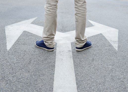 Man standing on two arrows on road going in opposite directions