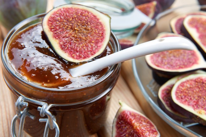 Jar of fig jam with figs on a plate beside it and one fig sitting on top of the jam jar.