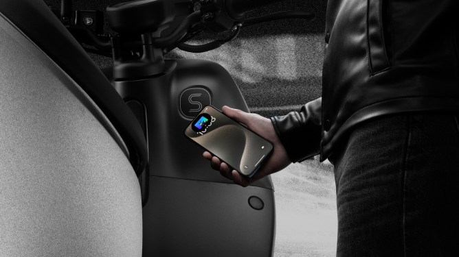 man's hand holding up iPhone next to Gogoro Smartscooter
