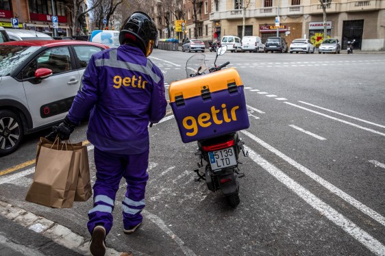 Getir delivery driver holding grocery bags and walking to Getir delivery bike