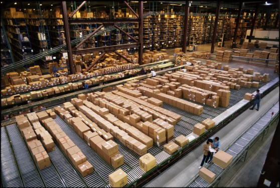Overview of a large industrial distribution warehouse storing products in cardboard boxes on conveyor belts and racks.