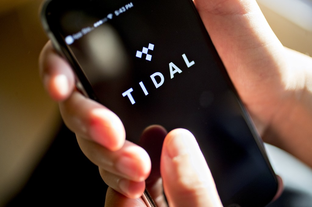 A person holding a phone displaying the Tidal logo