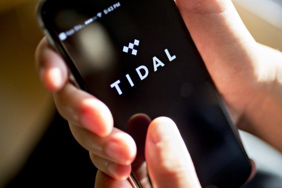 A person holding a phone displaying the Tidal logo