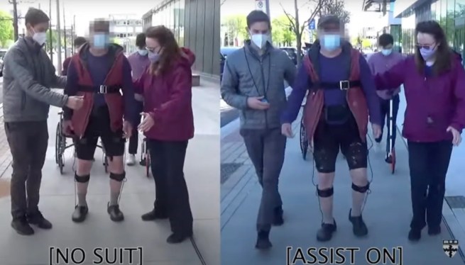 Photo showing man wearing robotic soft suit aided by two people