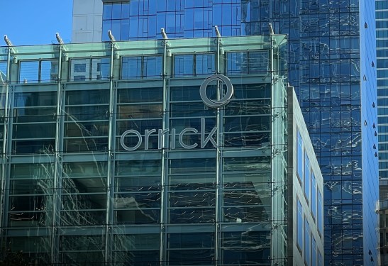 Low-angle view of the glass and steel Orrick Building, on a sunny day, with more glass-box skyscrapers in the background in San Francisco, California, October 4, 2022.