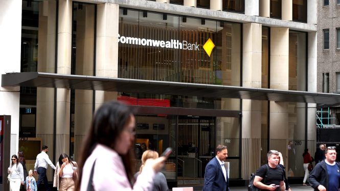 Pedestrians pass signage for Commonwealth Bank of Australia at a branch in Sydney, Australia.