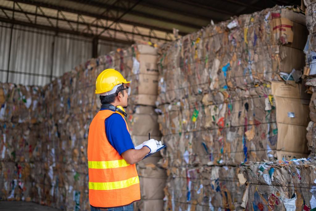 Man takes notes in front of bales of cardboard.