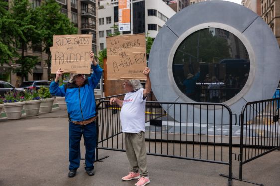 NEW YORK, NEW YORK - MAY 15: Two men hold signs in front of a video "Portal" art installation connecting New York City and Dublin, Ireland via a 24/7 video livestream which sits temporarily shut down in the Flatiron Plaza on May 15, 2024 in New York City. The "Portal", a Flatiron NoMad Partnership, has been temporarily shut down after two weeks for "inappropriate behavior" from a small group of individuals on both sides of the Atlantic. The livestream will once again be opened by the end of the week. (Photo by Spencer Platt/Getty Images)