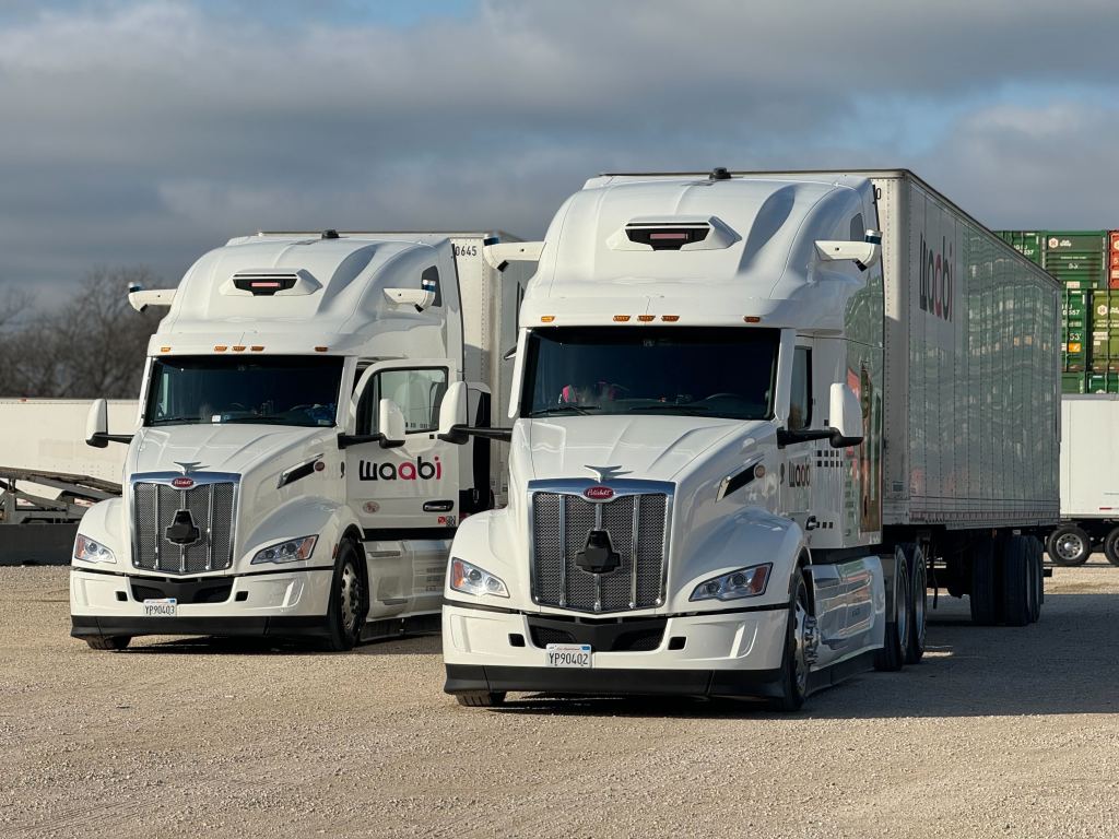 Front facing photo of two white Peterbilt heavy duty trucks with Waabi logo and branding.