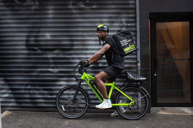 Side shot of food delivery worker on Whizz e-bike on NYC street in front of street mural
