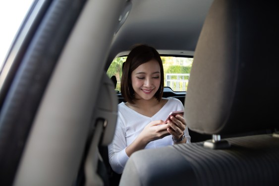 Asian teenager woman using a smartphone in back seat of car (Image Credits: comzeal/Getty Images)