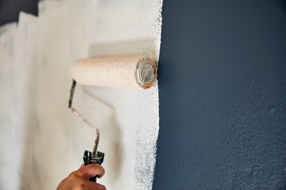 Man paints a wall white with a roller.