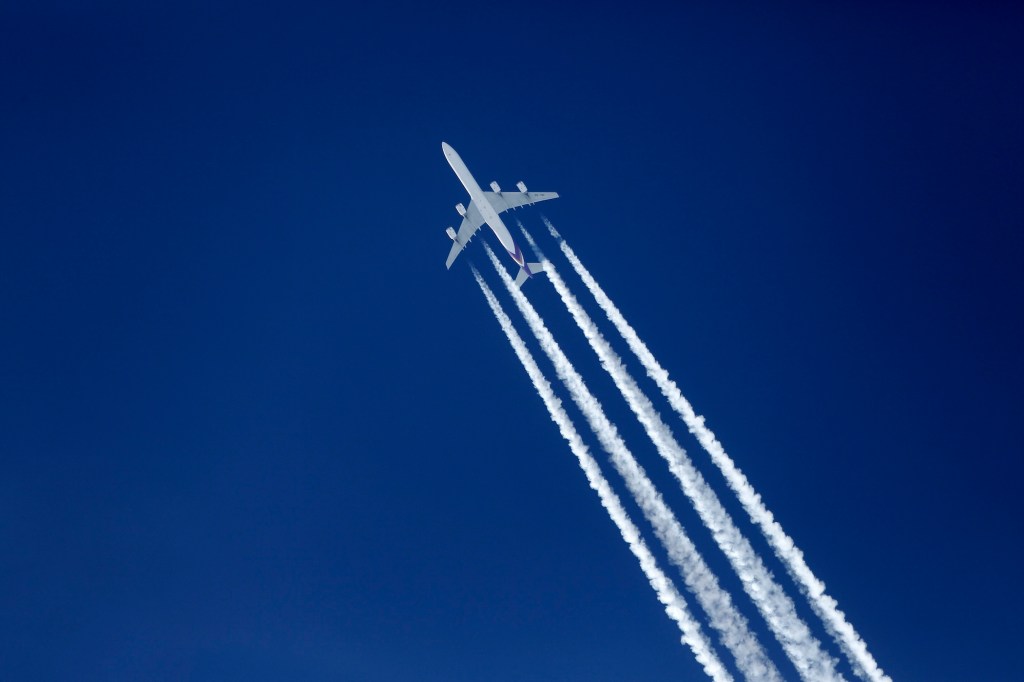 a photo of an airbus a340 with vapor trails behind it seen from the ground, with a deep blue sky