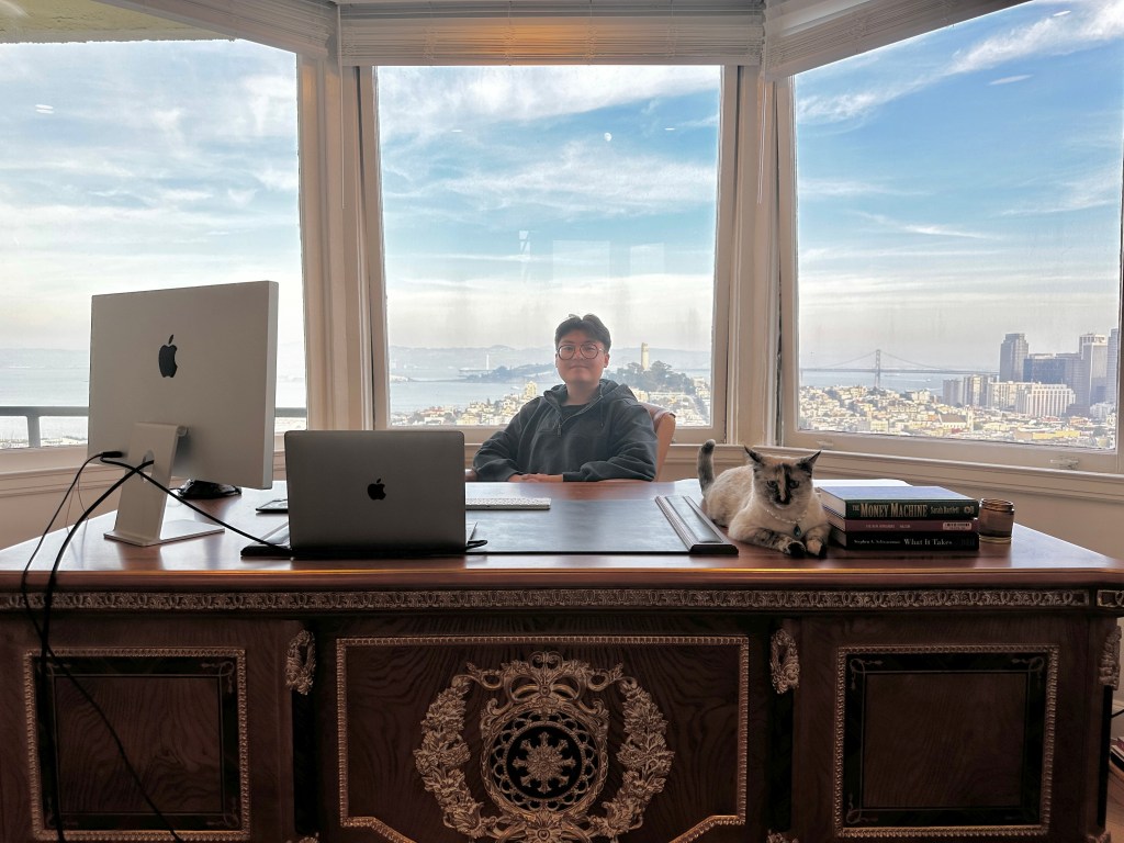 Koko Xs sitting at a large desk is front of large windows