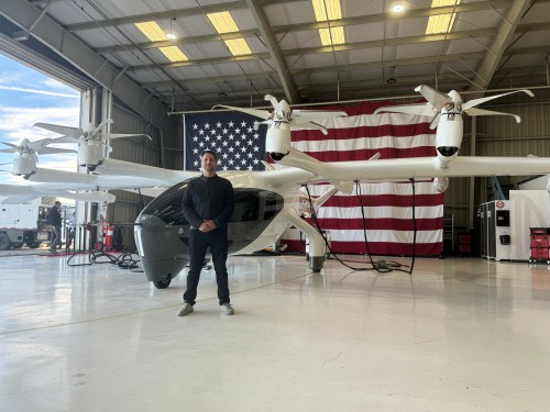 Archer CEO Adam Goldstein stands with one of his company's EVTOLs in front of a giant American flag.