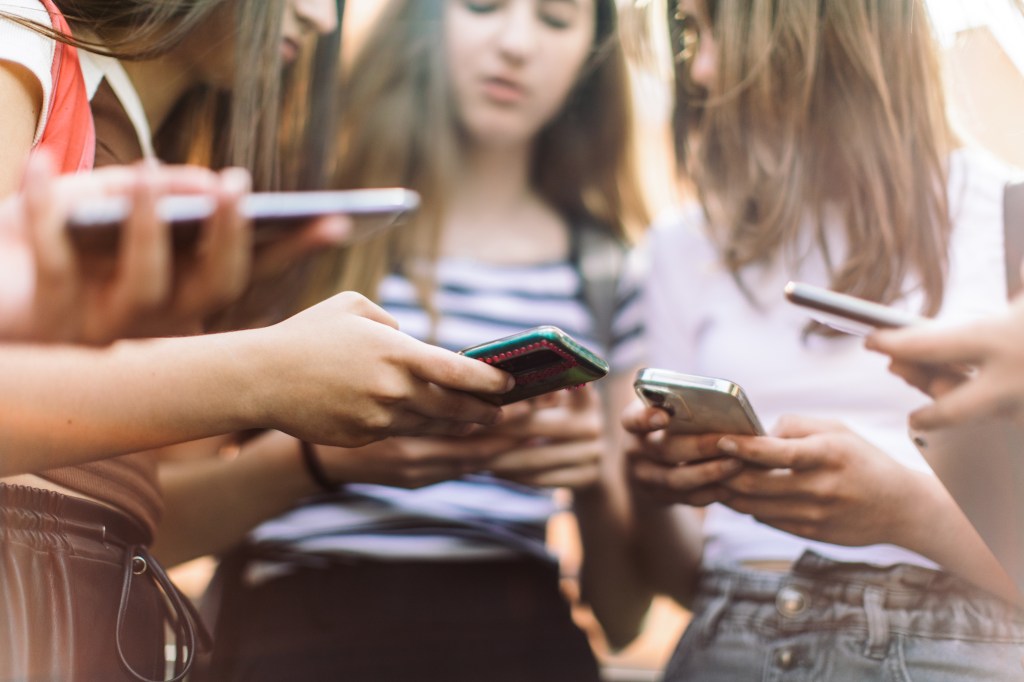 Group of teenage students standing in schoolyard and using mobile phones. They are very happy and playful.