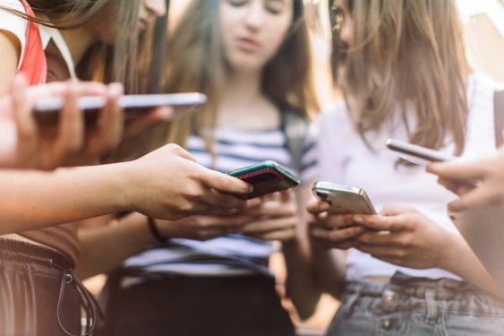 Group of teenage students standing in schoolyard and using mobile phones. They are very happy and playful.