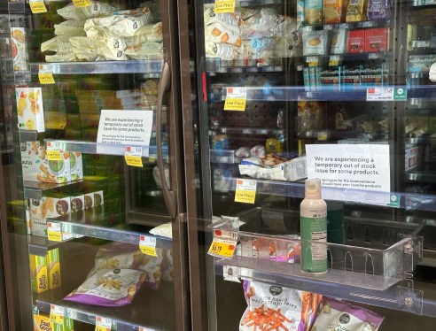 a photo of the frozen and refrigerated section at a local Whole Foods, with empty spaces, and signs warning of an out-of-stock issue.